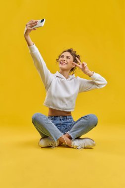 Yukarıdan selfie çeken güzel bir kız. Loto pozisyonunda oturan, gülümseyen, selam veren, akıllı telefon tutan güzel genç bir kadın. Gençlik ve modern hayat kavramı,