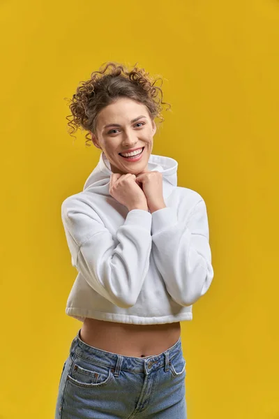 stock image Front view of pretty girl with curly hair standing, smiling. Slim beautiful young woman holding by hands, looking at camera, posing. Isolated on yellow studio background.