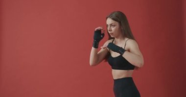 Güzel, esmer bir sporcunun yan görünüşü. Kapalı alanda çalışıyor, boks yapıyor, tekme atıyor, ileriye bakıyor. Zayıf, formda, esneme hareketleri olan, spor giyimli bir kadın. Sağlıklı yaşam kavramı.