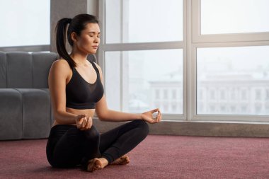 Loto pozisyonunda meditasyon yapan genç bir kadının yan görüntüsü. Esmer, güzel bir kadın, gözleri kapalı, yoga yapıyor. Yoga yapma ve uyum içinde yaşama kavramı.