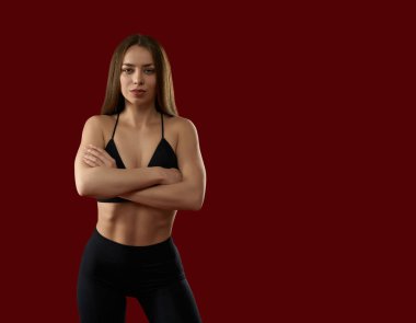 Seksi sporcu kadın kameraya çapraz ellerle bakıyor. Siyahlı baştan çıkarıcı kadın antrenör kırmızı stüdyo arka planında poz veriyor..