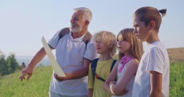 Bir grup turistin birlikte yürüyüşünü, ayakta duruşunu, gökyüzüne bakışını. Sırt çantalı yaşlı adam harita tutuyor, ufku gösteriyor, konuşuyor, gülümsüyor. Turizm ve takım ruhu kavramı.