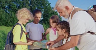 Ayakta duran çocukların, haritaya bakan yaşlı adamın pusula kullanması, yön göstermesi, arama rotası. Dağlarda yürüyüş yapan, birlikte kamp yapan turistler. Turizm kavramı,