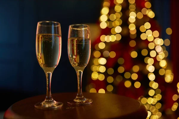 Close up of two glasses of champagne, sparkling wine standing on table. People celebrating new year in studio decorated with christmas tree. Concept of new year and holiday.