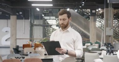 Mutlu, genç satıcı, mimar, tasarımcı mobilya mağazasında duruyor, klasörü tutuyor. Esmer satıcı, tasarımcı, mimar, etrafa bakınıyor. Kentsel yaşam tarzı kavramı.