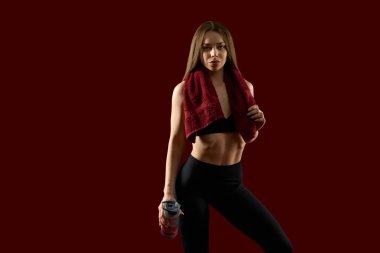 Eğitimden sonra boynunda havluyla vitamin ya da suyla titreten çekici esmer kadın. Kırmızı stüdyoda uzun saçlı, protein içeceğiyle poz veren formda bir bayan antrenör.. 