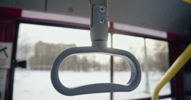 Close up of grey handle on empty bus. Bus stopping, city with house and trees on background in window, blurred, sunny, sunset, evening. Concept of transport and urban settings.