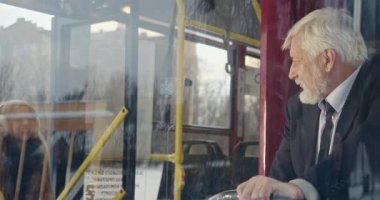 Close up of old driver greeting passengers on bus. Male with grey hair looking at young girl wearing earphones, smiling, small boy waving. Concept of modern life and transport.