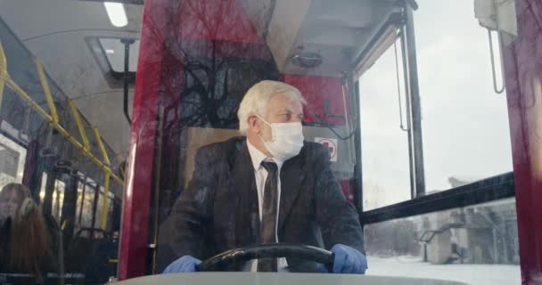 司机戴着口罩和医用手套掌舵的前视图 头发灰白的老人开公共汽车 望着车窗 保护着恐怖的验尸官 检疫措施的概念 — 图库视频影像