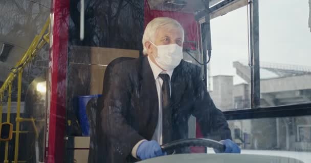 司机坐在巴士上 戴着口罩和医用手套的前视图 全球大流行病期间驾驶公共交通工具的老年男性白发 大流行病计量概念 — 图库视频影像