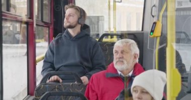 Front view of passengers traveling by public transport. Boy with earphones, listening to music, old man with grey hair and beard, girl in white hat sitting. Concept of routine.