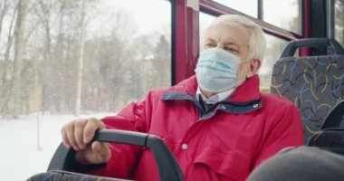 Side view of old man wearing medical mask sitting on bus. Passenger with grey hair protecting from covid-19, following quarantine measures. Concept of modern global pandemic.