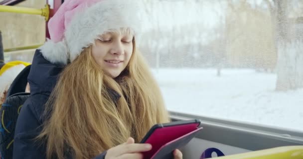 画面上のタブレットを使用してクリスマスの帽子の女の子のフロントビュー 若いブロンドの女性は 笑みを浮かべて座って 画面を見て テキストメッセージ チャット ブラウジング 現代の現実の概念 — ストック動画