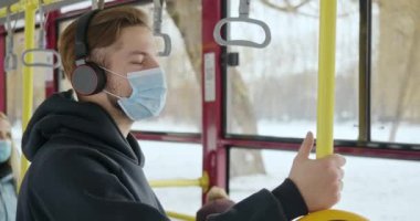 Tıbbi maske kullanarak otobüsteki yolcuların yan görüntüsü. Sarı pipo tutan genç bir adam, kulaklıkla müzik dinliyor, covid-19 'dan koruyor. Modern karantina gerçekliği kavramı.