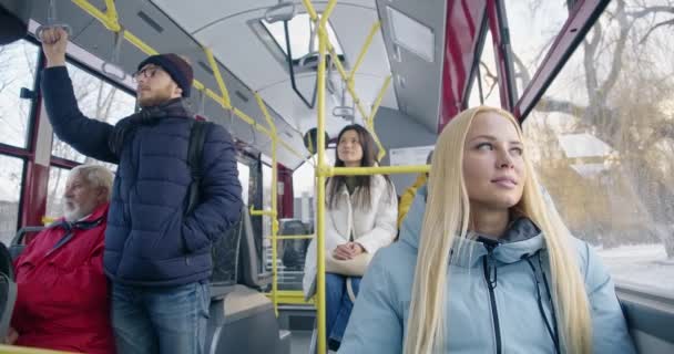 乘客坐在巴士上 旅行的前景色 金发姑娘望着窗户 面带微笑 戴眼镜的男孩子拿着把手 白发苍苍的老人坐着 城市生活的概念 — 图库视频影像