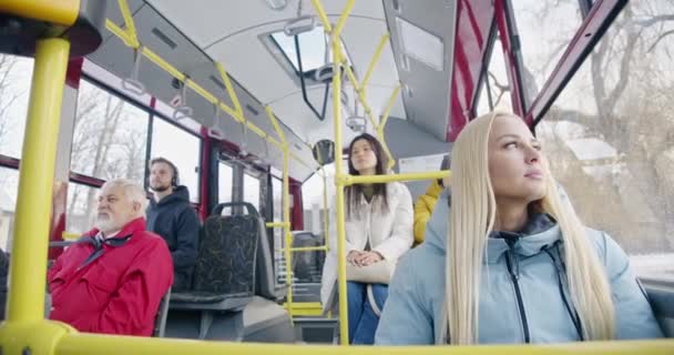 乘坐公共汽车 乘坐公共交通工具旅行的乘客的前景 漂亮的金发姑娘望着窗户 穿着红色夹克的老人在等着 城市生活的概念和常规 — 图库视频影像