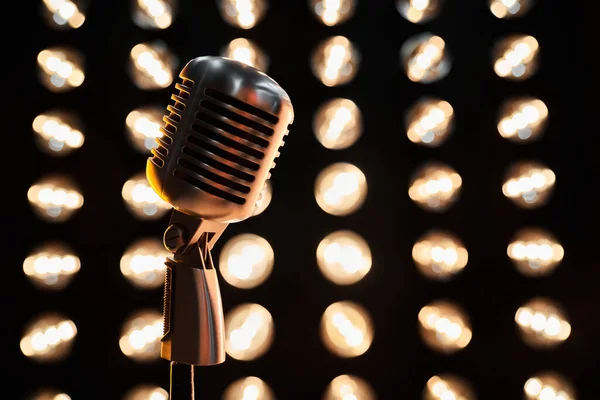 Retro metal microphone in front of abstract blurred spotlights on black background. Close up of vintage mic against dark sparkling bokeh backdrop, with copy space. Concept of music, podcast.