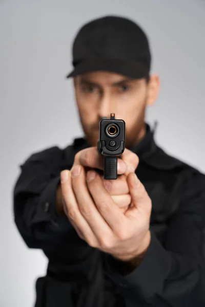 无法辨认的便衣警察瞄准了 把注意力集中在室内摄像头上 近距离的黑色武器 由模糊的警察轮廓持有 灰色背景 目标的概念 — 图库照片