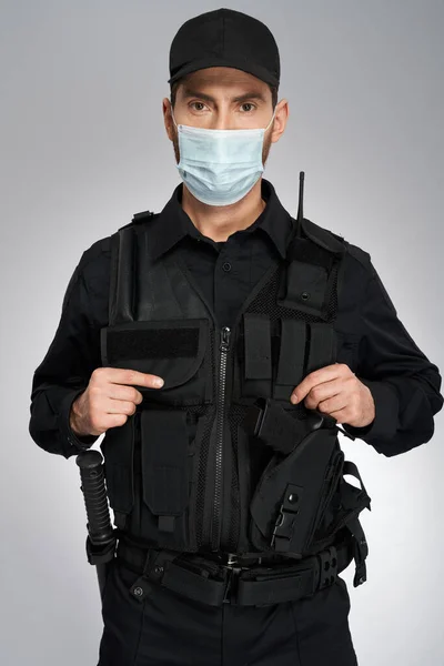 年轻的高加索警察戴着防护面具看着摄像机 身着防弹背心装扮的自信警官形象 在灰色工作室背景下被隔离 工作概念 — 图库照片