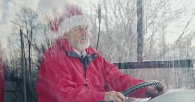 Noel şapkası takan otobüs şoförünün yan görüntüsü. Gri saçlı ve sakallı yaşlı adam miğferde el ele tutuşuyor, ileriye bakıyor. Şehir hayatı, Noel ve kutlama kavramı. 