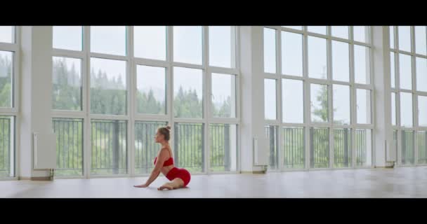 ジムでヨガを練習しながら 赤いスポーツ服を着た若い女性 強く健康な女性が床に体を伸ばします 人と運動の概念 — ストック動画
