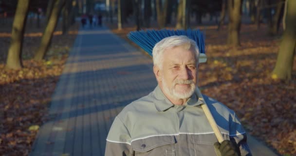 Starszy Konsjerż Mundurze Rękawiczki Pozujące Jesiennym Parku Miejskim Niebieską Miotłą — Wideo stockowe