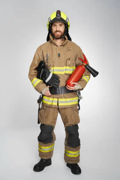 Kasklı Genç Itfaiyeci Stüdyoda Yangın Söndürücü Tutuyor Tfaiyeci Üniforması Giyen — Stok fotoğraf