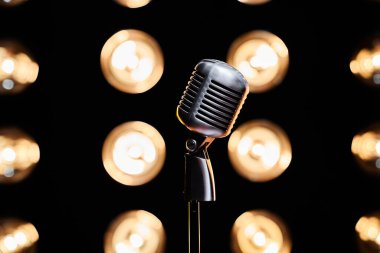 Arka planda ampul ışıkları olan boş bir sahnede bir retro mikrofon. Aydınlatılmış stüdyodaki gümüş mikrofonun yakın görüntüsü. Performans, gösteri, müzik kavramı.