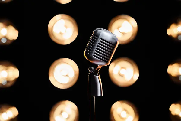 One retro microphone on empty stage with bulb lights on backdrop. Close up view of silver mic on stage in illuminated studio. Concept of performance, show, music.