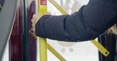 Otobüsteki stop düğmesine basan yolcunun arka görüntüsü. Sarışın, uzun saçlı, sarı saplı, mavi ceketli. Günlük rutin ve gerçeklik kavramı.