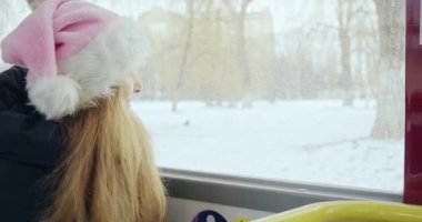 Pencereden bakan, el sallayan, gülümseyen genç bir kız. Otobüste annesi ve çocuğu olan, Noel şapkalı, neşeli sarışın kız. Noel ve Yeni Yıl kavramı.
