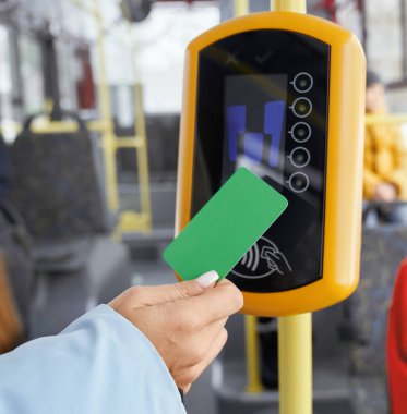 Kamu aracında binerken yeşil ödeme kartını onaylayıcının önünde tutan kadın eli. Ulaşım terminalini kullanarak el görüntüsünü kapat. Modern elektronik aygıtlar kavramı.