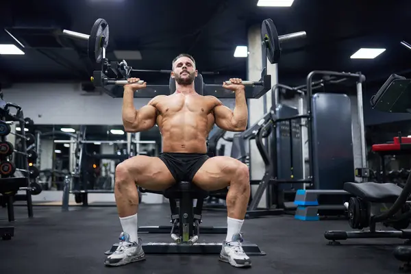 ジムでトレーニング装置で運動をしているダークヘアの筋肉男性 トレーニング中にスポーツ機器を使用して 強い男性アスリートの低角度ビュー スポーツ ウェイトリフティングコンセプト ロイヤリティフリーのストック写真