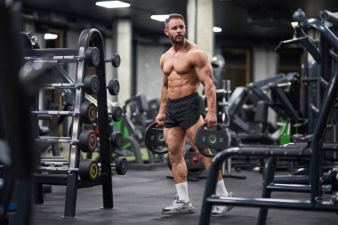Spor salonunda halterci halter için tabak tutuyor. Kaslı sporcunun yuvarlak tabaklar taşıması, egzersiz yapması, tırlara ve askılara karşı egzersiz yapması. Ağırlık kaldırma kavramı. 