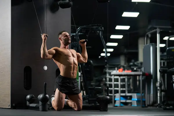 Skoncentrowany Przystojny Sportowiec Klęka Podczas Wykonywania Ćwiczeń Dla Bicepsów Siłowni Zdjęcie Stockowe