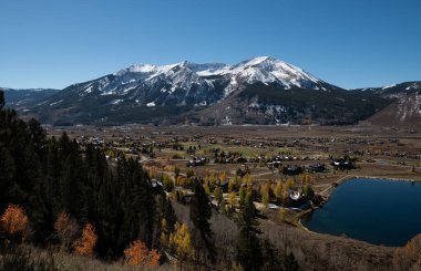 Aerial view of Crested Butte Town and properties with fall colors, a mountain background, and sunny blue skies clipart