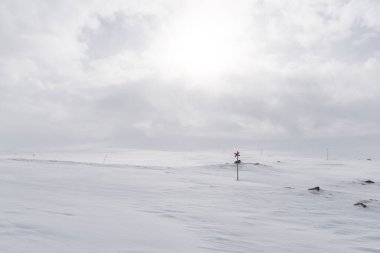 A lone ski trail marker in Sweden with the sun shining behind