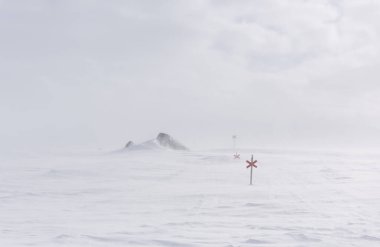 High winds blow snow across a ski touring track in the Swedish Mountains. Ski trail markers lead the way on ahead.