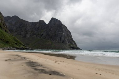 Kuzey takımadalarındaki Kvalvika plajında siyah kumla beyaz kumların karışımı. Dağların arkasında fırtına bulutları beliriyor