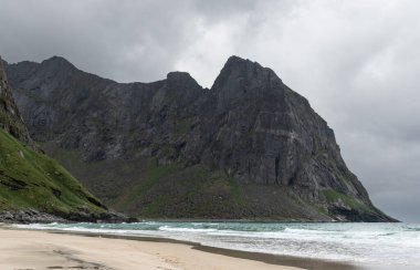 Blues denizlerinin üzerinde yükselen bir dağ ve Lofoten 'deki Kvalvika plajında karanlık gökyüzünün önünde