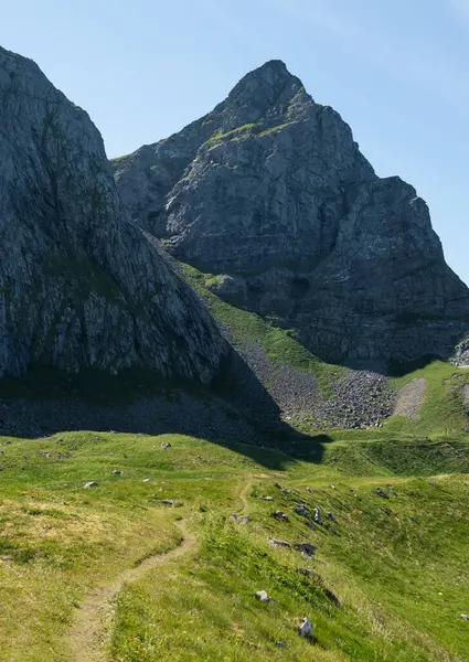 stock image A coastal trail winds toward the base of tall rock formations on Vaeroy, Lofoten, Norway