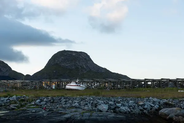 Lofoten Takımadası 'ndaki Vaeroy adasındaki balık kurutma tezgahlarının önünde bir tekne karada duruyor.