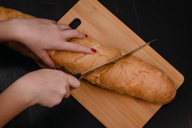 Kadın elleri tahta bir arka planda ekmek kesiyor.