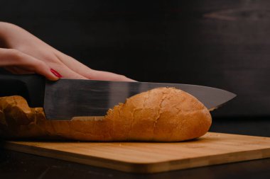 Kadın elleri tahta bir arka planda ekmek kesiyor.