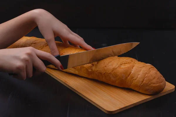 Frauenhände Schneiden Brot Auf Einem Schneidebrett Auf Einem Holzhintergrund — Stockfoto