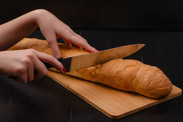 女性的手在木头背景的刨花板上切面包 — 图库照片