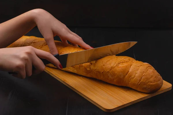 女性的手在木头背景的刨花板上切面包 — 图库照片