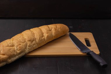Beyaz ekmek ve bıçak tahta bir arka planda kesme tahtasının üzerinde yatıyor.