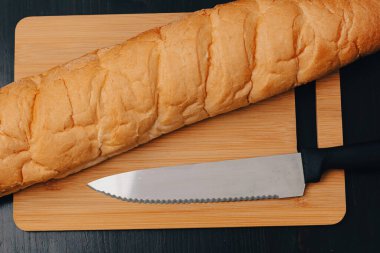 Beyaz ekmek ve bıçak tahta bir arka planda kesme tahtasının üzerinde yatıyor.