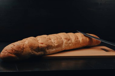 Beyaz ekmek ve bıçak tahta bir arka planda kesme tahtasının üzerinde yatıyor.